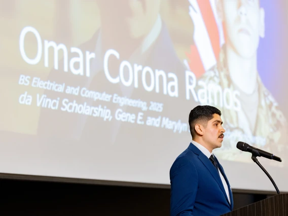 A young man with brown hair and a brown mustache reads a speech.