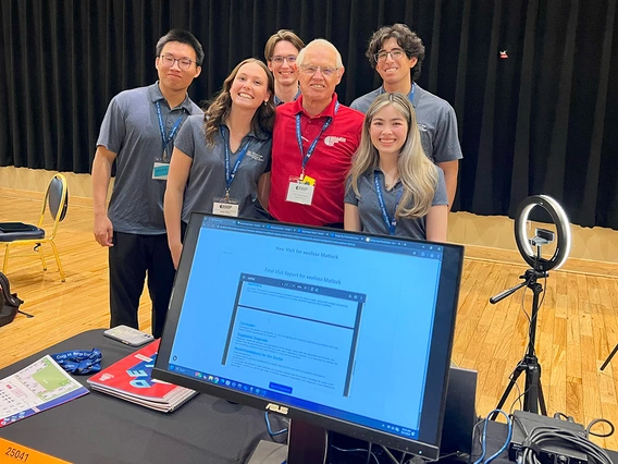 Five students in gray shirts take a photo with an older man.