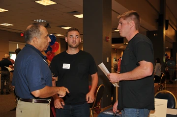 Three men talking in a ballroom during an open house event