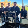 Six students stand behind a plexiglass cube holding a device.